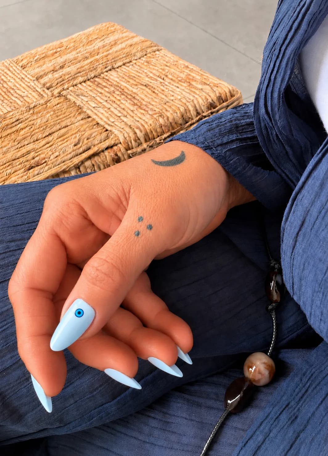Sky-blue stiletto nails with an evil-eye accent against soft denim.