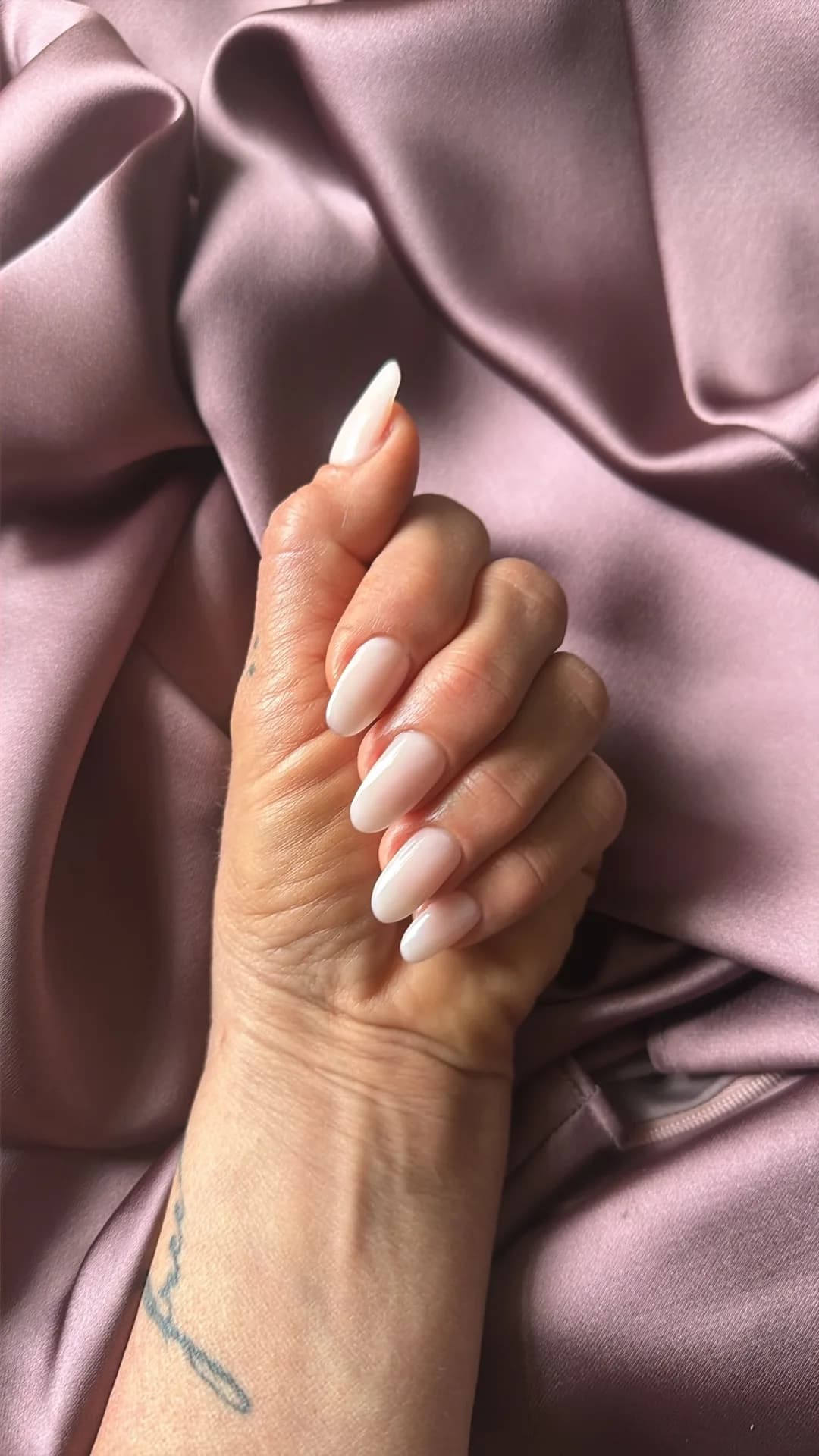 Milky-white almond nails draped over rose-mauve satin.