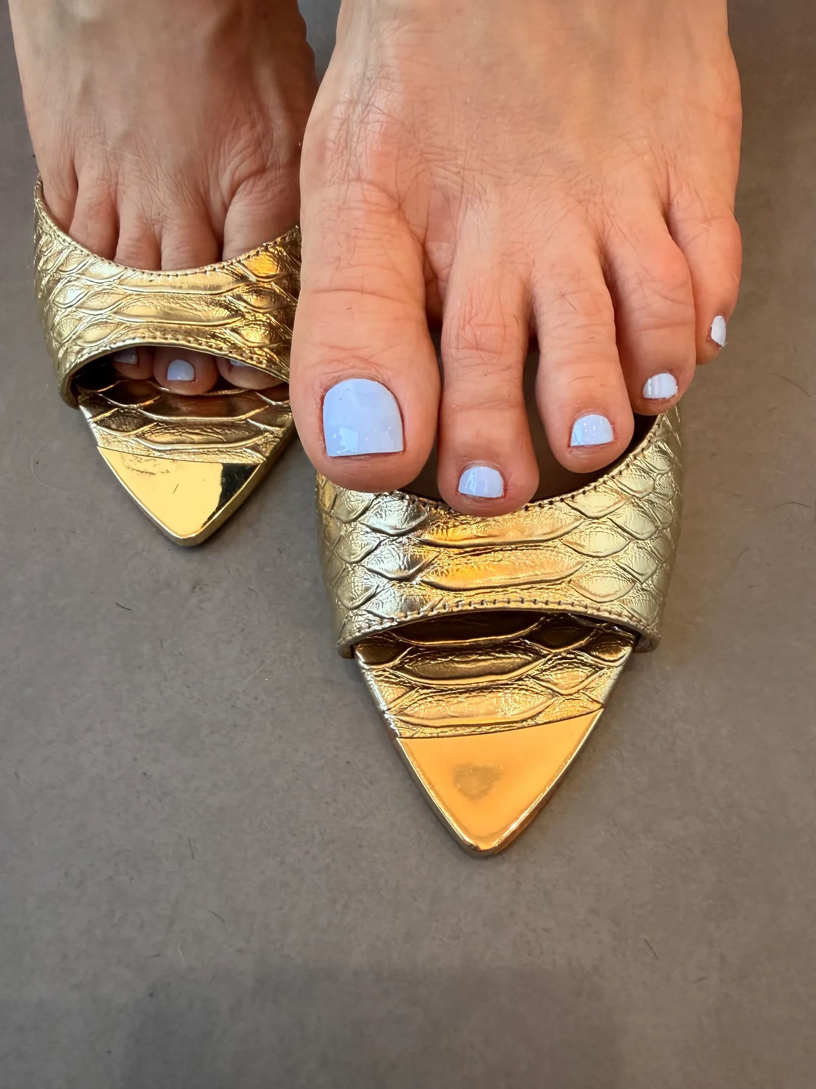 Soft lilac-white pedicure in pointed gold mules.