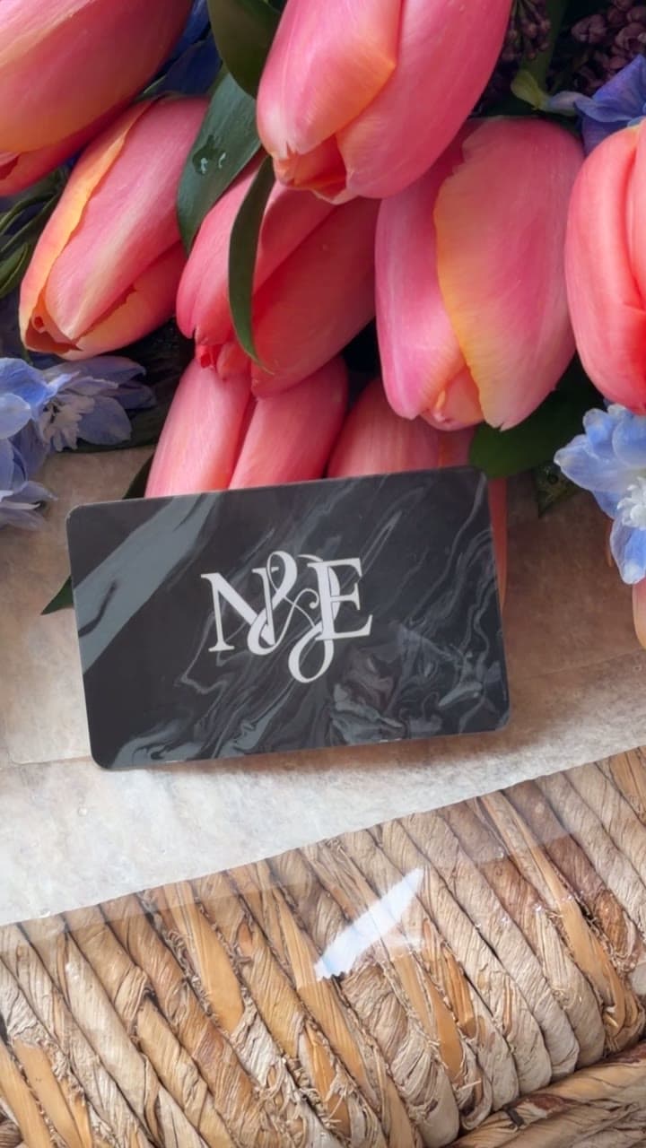 An N&E gift card resting among coral tulips and blue delphinium.
